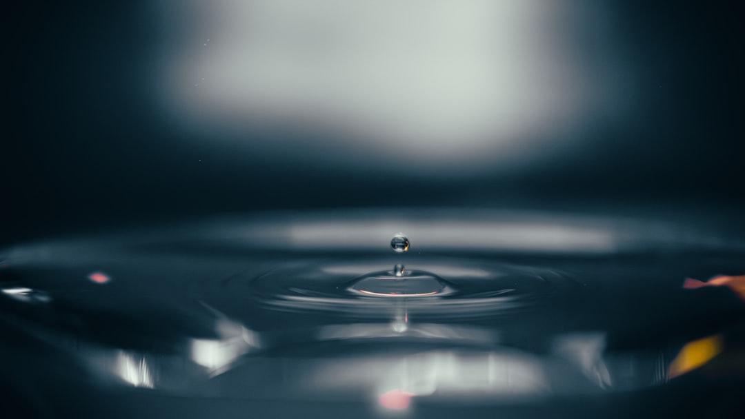 A clean, minimalist photo of a single water drop hitting a calm surface, creating perfect, expanding concentric circles, visually representing the ripple effect.